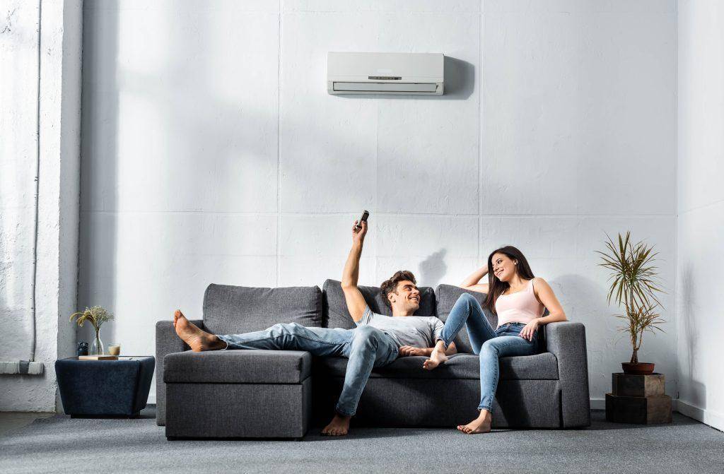 Afbeelding van man en vrouw zittend op een grijze bank die hun airconditioner aanzetten met afstandbediening.